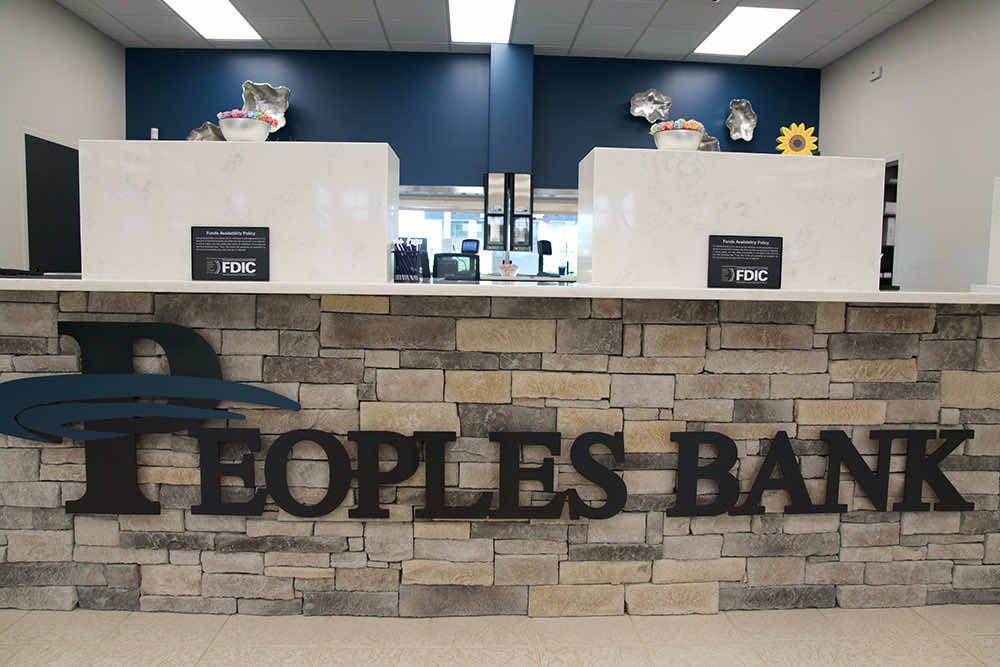 Teller counter inside a Peoples Bank branch with the bank logo mounted on a stone wall