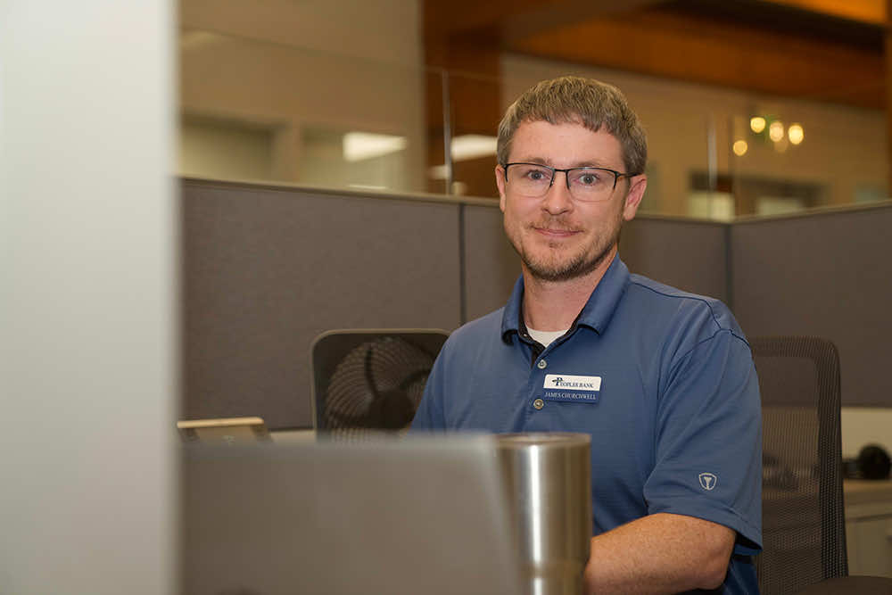 A Peoples Bank employee working at a computer in an office cubicle