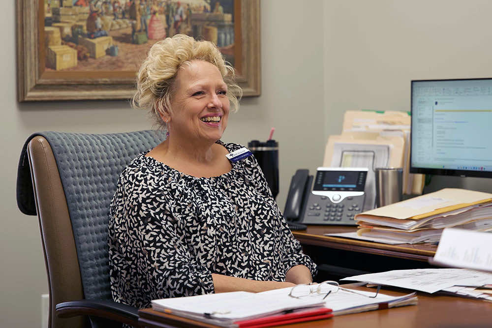 A Peoples Bank employee laughing at a desk stacked with files